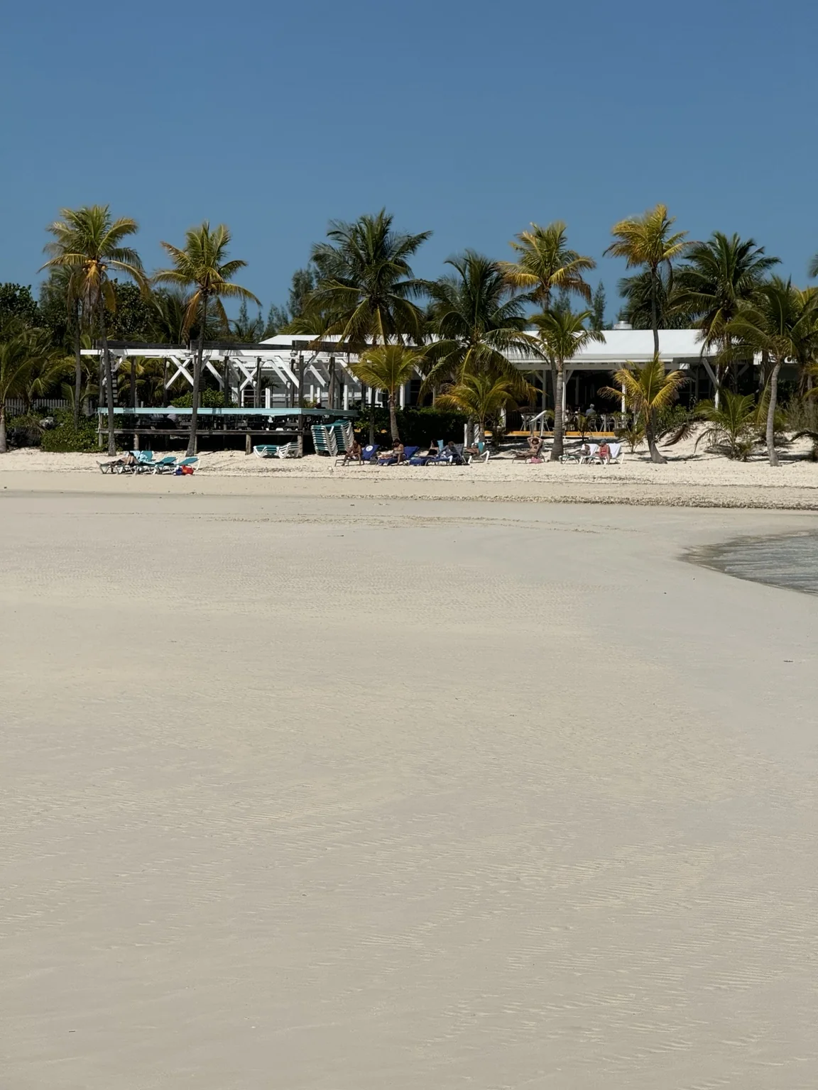 A broad sandy Grand Bahama beach with a low white beachfront building and palm trees beyond