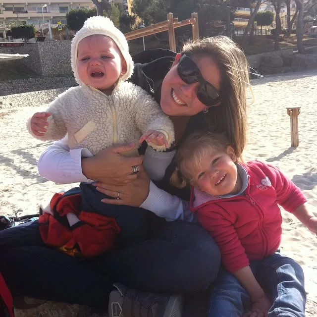 Pamela holding baby Junior while Patricia leans against her on a Mallorca beach